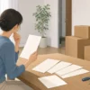 一人暮らしをやめて実家に帰るか、書類と引っ越し箱を前に考える様子